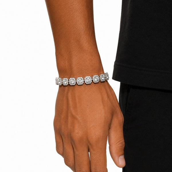 A close-up of a person's wrist wearing a silver-toned tennis bracelet set with clear round-cut cubic zirconia, shown against a white background with a black shirt visible on the right.