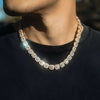 A close-up lifestyle shot of a man wearing a chunky, gold-toned tennis chain necklace over a black crewneck shirt.