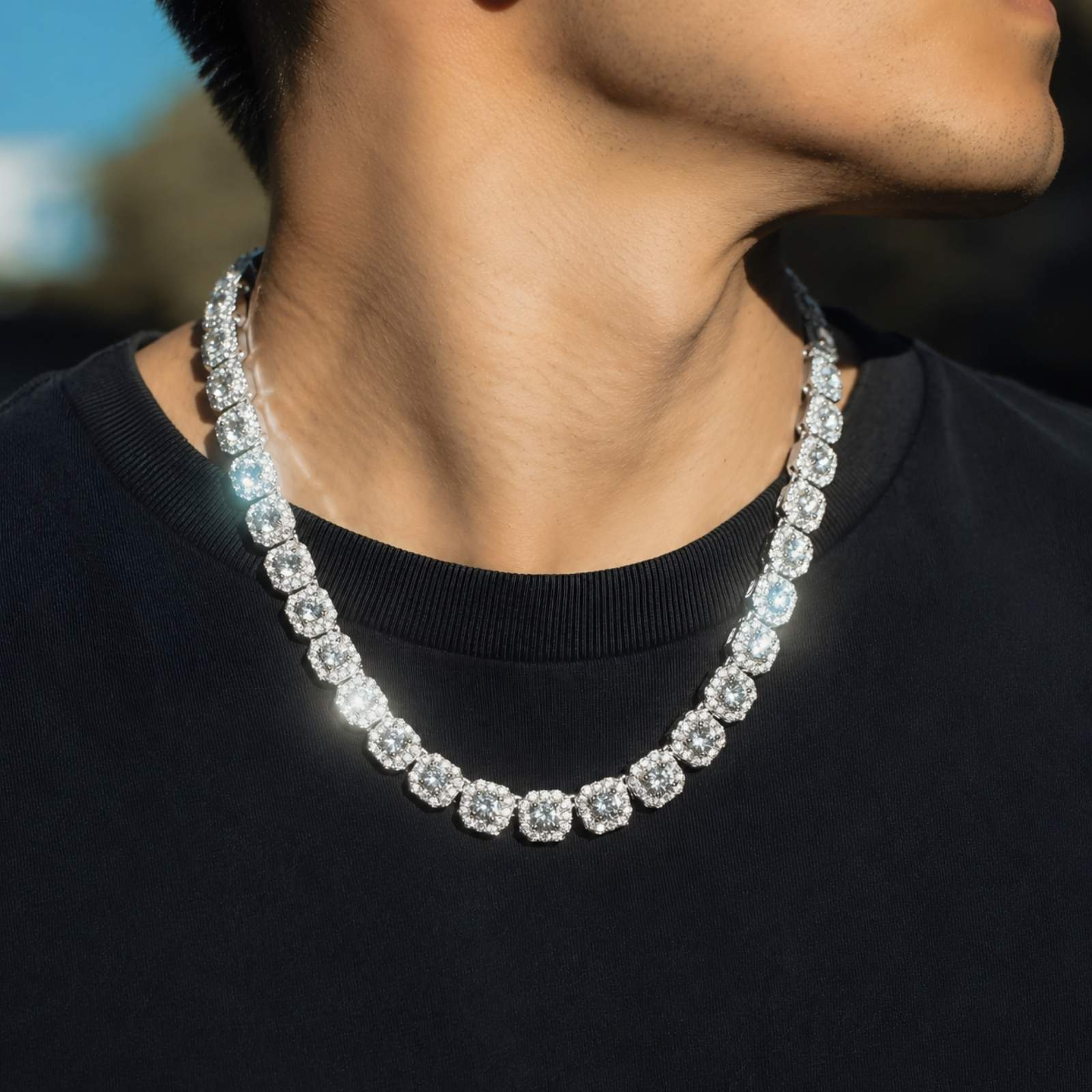 A close-up lifestyle shot of a man wearing a silver-toned cubic zirocnia tennis chain necklace over a black t-shirt.