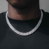 A close-up of a man wearing a thick silver Cuban link chain necklace with pavé stones, styled over a black t-shirt.