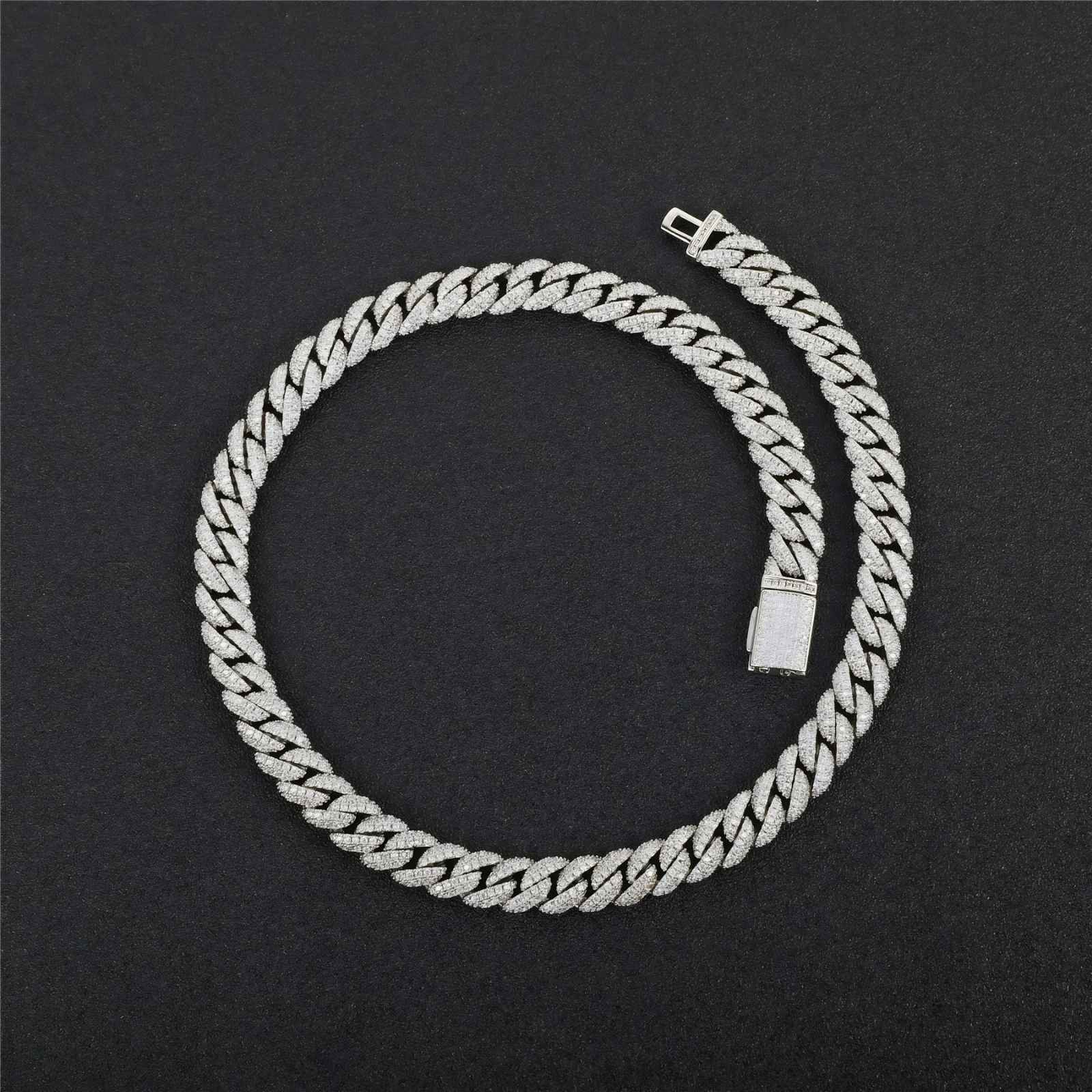 A silver-toned Cuban link chain necklace, sometimes referred to as an 'ice chain,' coiled on a dark textured background. The links are detailed with small clear stones, giving them a sparkling finish.
