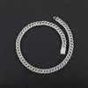 A silver-toned Cuban link chain necklace, sometimes referred to as an 'ice chain,' coiled on a dark textured background. The links are detailed with small clear stones, giving them a sparkling finish.