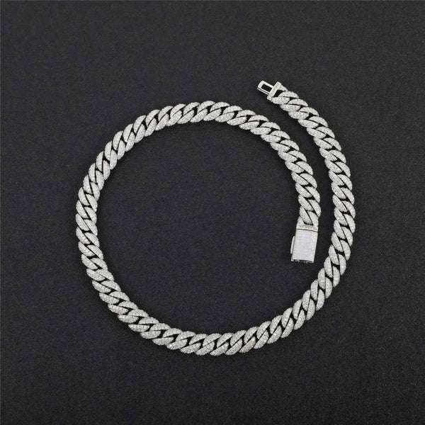 A silver-toned Cuban link chain necklace, sometimes referred to as an 'ice chain,' coiled on a dark textured background. The links are detailed with small clear stones, giving them a sparkling finish.
