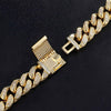 A gold-toned Cuban link chain with pavé-set clear stones, shown in close-up on a dark textured background. The clasp is visible