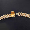 A gold-tone Cuban link bracelet paved with small clear stones, shown on a dark textured background. The clasp is open to display the interior mechanism.
