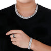 A close-up of a person wearing a chunky silver Cuban link chain necklace, matching silver bracelet, and silver ring, styled with a black t-shirt against a white background.