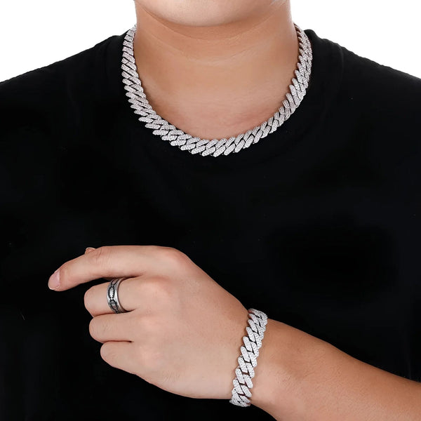 A close-up of a person wearing a chunky silver Cuban link chain necklace, matching silver bracelet, and silver ring, styled with a black t-shirt against a white background.