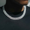 A close-up of a man wearing a thick silver-toned Cuban link chain necklace paved with small clear stones, paired with a black t-shirt.