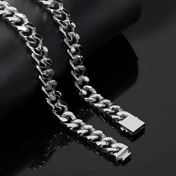 A close-up of a shiny silver Cuban link chain draped over a black cylindrical display stand on a dark reflective surface.