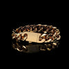 A gold-toned chunky chain link bracelet with a polished rectangular clasp, displayed on a reflective black surface against a solid black background.