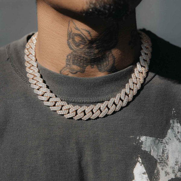 A close-up of a person wearing a thick, chunky silver-toned Cuban link chain necklace covered in small clear stones, paired with a dark gray t-shirt.
