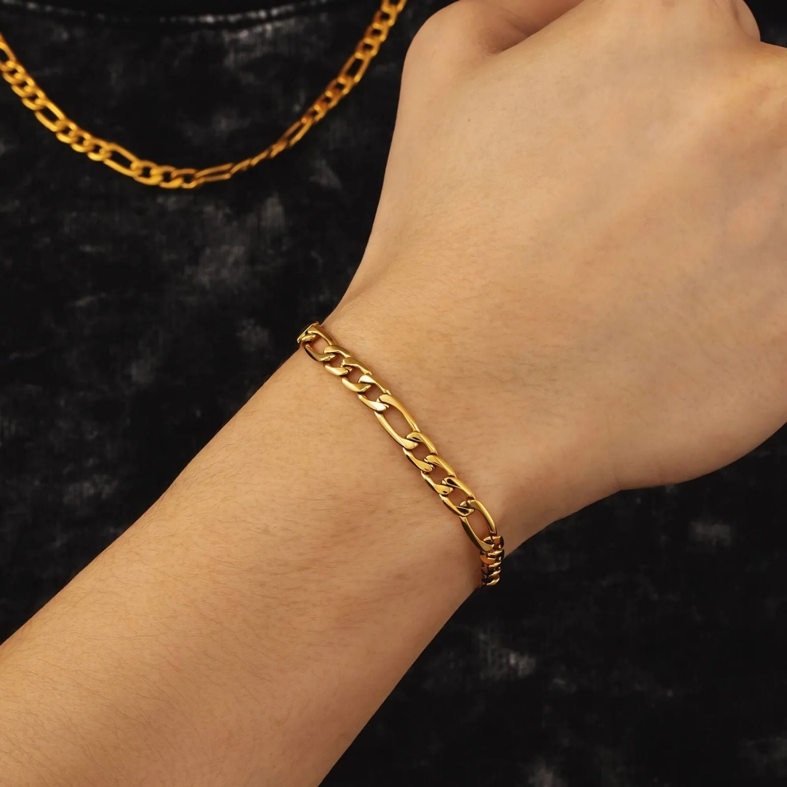 Gold chain and bracelet on a model against a dark background