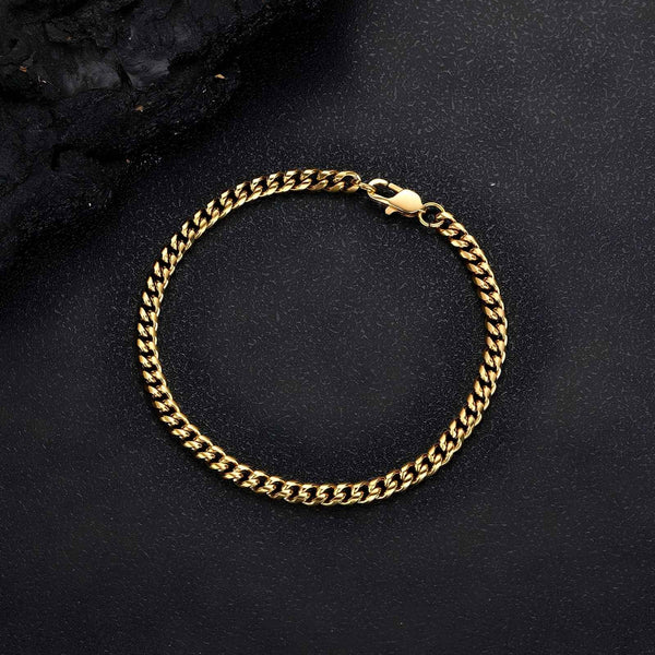 A gold-toned curb chain bracelet with a lobster clasp, displayed on a textured black background.