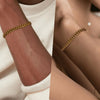 Gold chain bracelet on a wrist with a neutral background