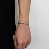 Person wearing a silver rope bracelet on a plain background