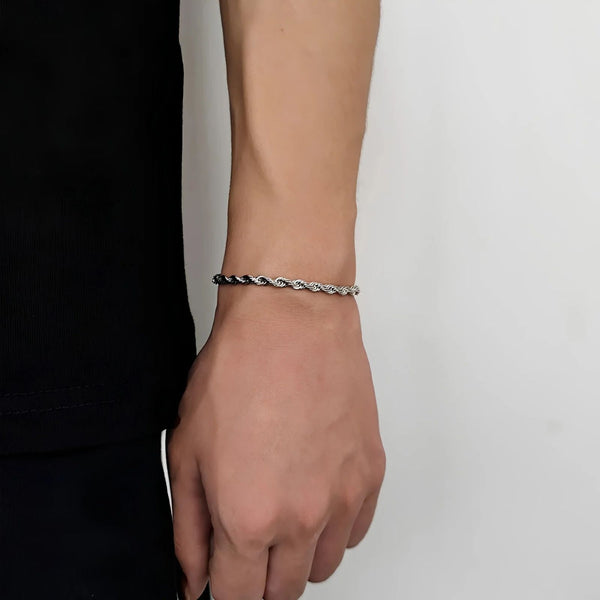 Person wearing a silver rope bracelet on a plain background