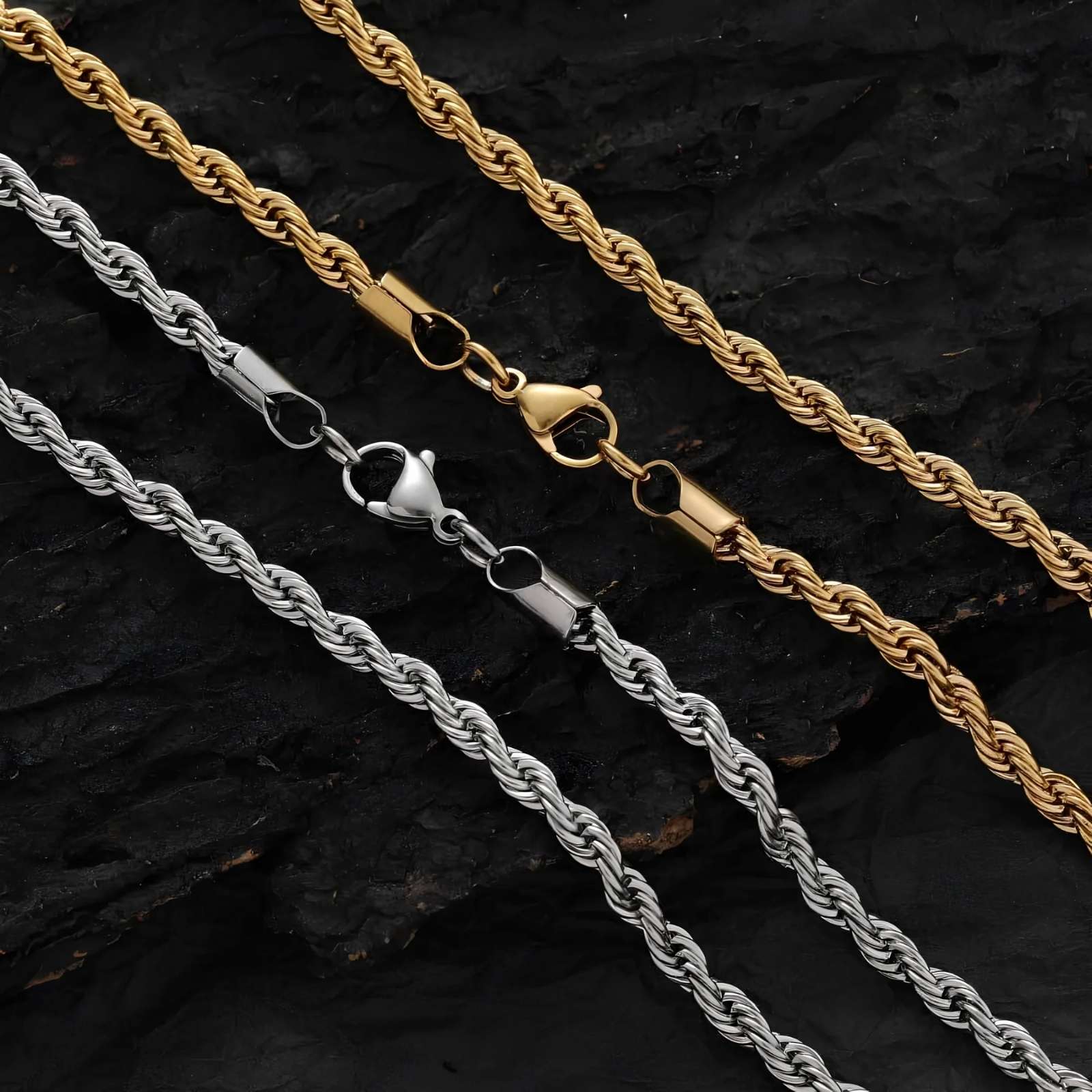 Two rope chains, one gold and one silver, on a dark textured surface.