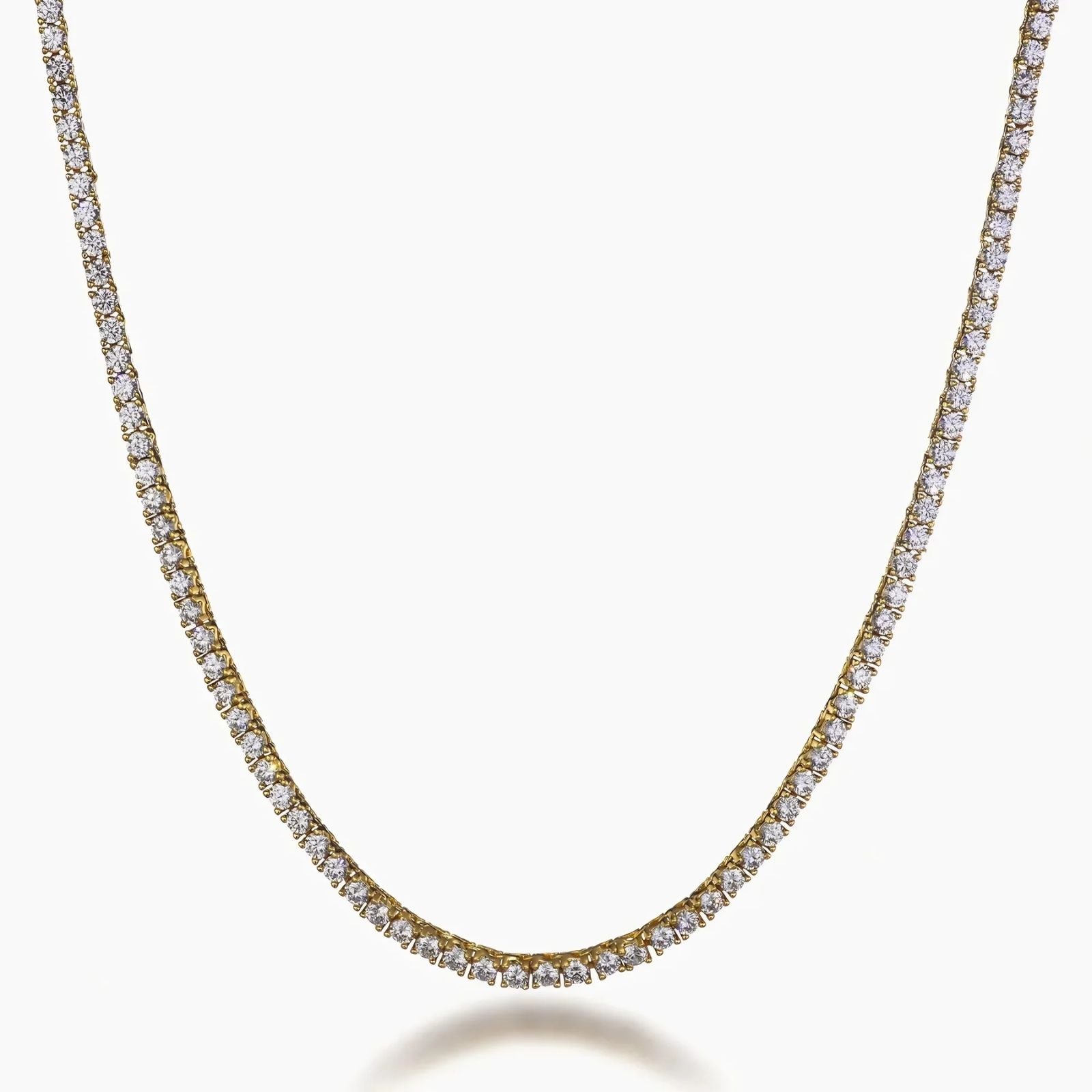 A gold tennis necklace paved with small clear cubic zirconia stones, shown in a curved U-shape against a light gray background.