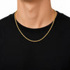 A close-up of a person's neck and upper chest wearing a gold rope chain necklace over a black crewneck t-shirt, against a plain white background.