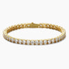 A gold tennis bracelet featuring a continuous row of round-cut clear cubic zirconia in a prong setting, shown against a plain light gray background.