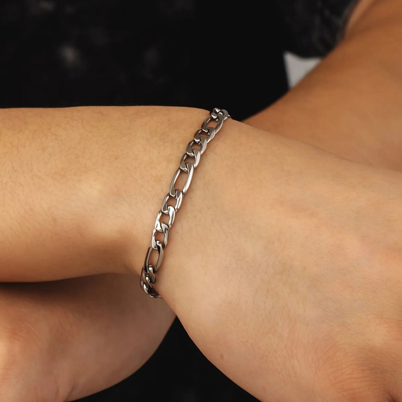 A close-up of a polished silver chain link bracelet worn on a person's wrist, set against a dark background.