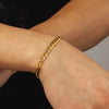 Gold chain bracelet on a wrist with a neutral background