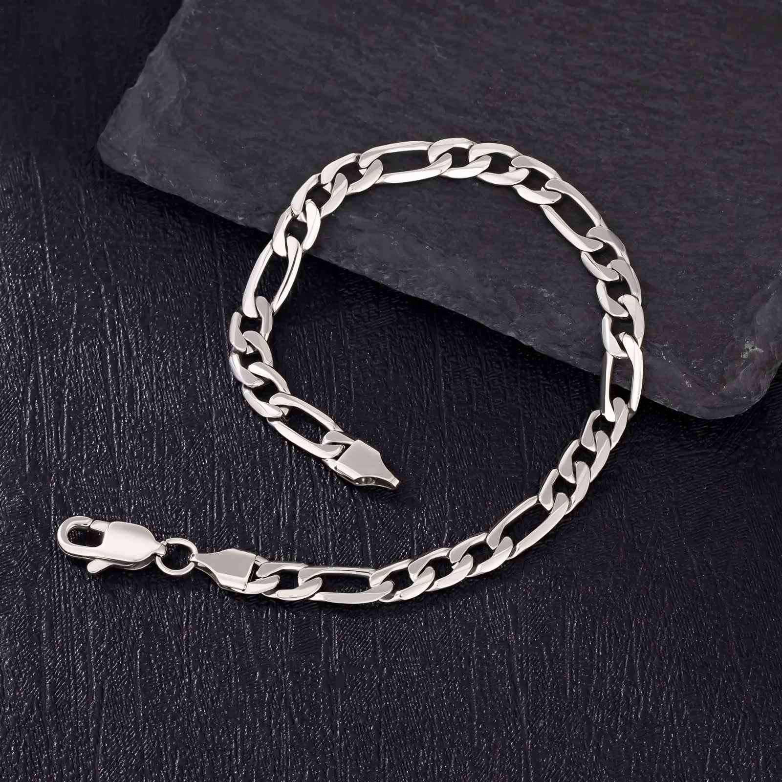 Silver figaro chain bracelet on a dark stone surface