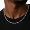 A close-up of a man's neck and chest wearing a silver-toned curb chain necklace over a black crew-neck t-shirt.