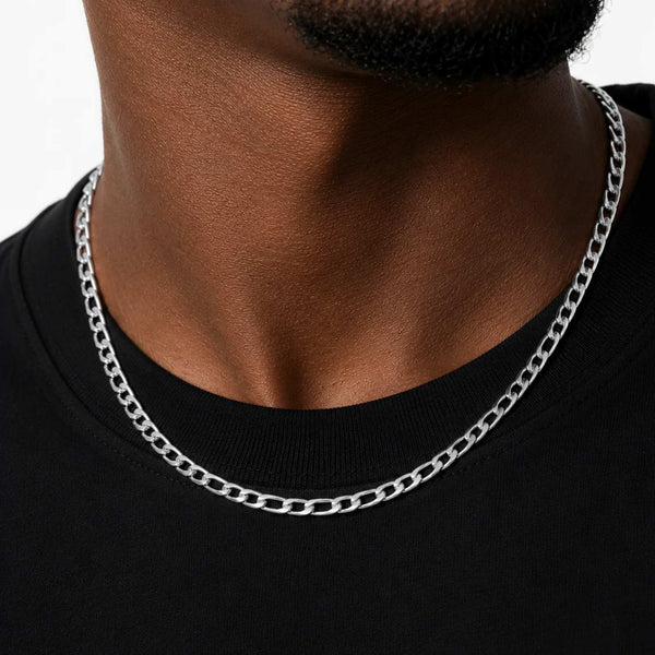 A close-up of a man's neck and chest wearing a silver-toned curb chain necklace over a black crew-neck t-shirt.