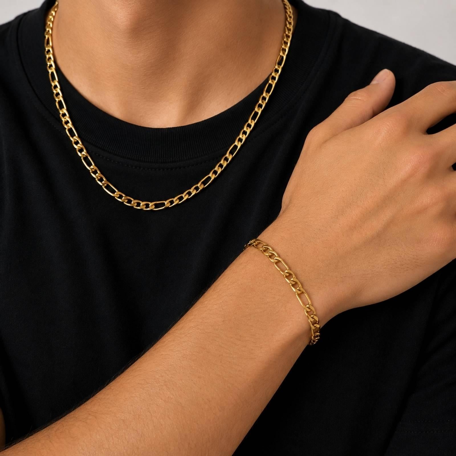 A close-up of a person wearing a gold chain necklace and a matching gold chain bracelet, with the person wearing a black t-shirt.