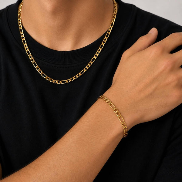 A close-up of a person wearing a gold chain necklace and a matching gold chain bracelet, with the person wearing a black t-shirt.