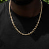 A close-up of a gold-toned Cuban link chain necklace worn by a person in a black t-shirt.
