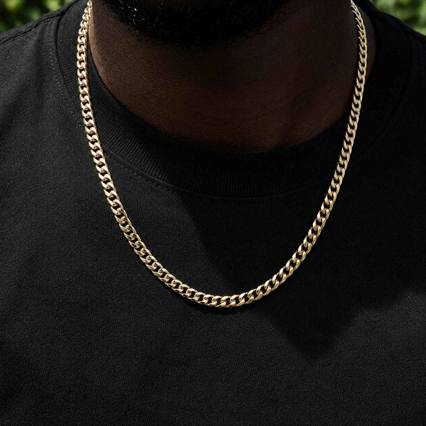 A close-up of a gold-toned Cuban link chain necklace worn by a person in a black t-shirt.
