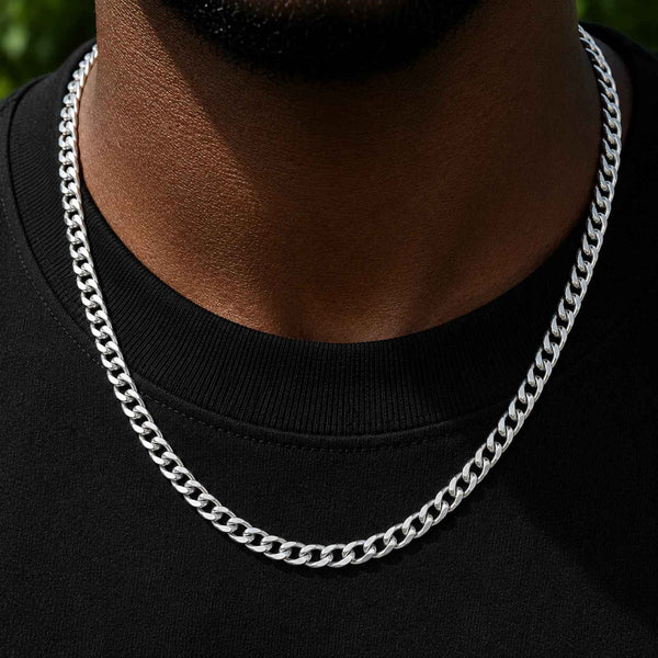 A close-up of a man's neck and chest wearing a thick, polished silver Cuban link chain necklace over a black t-shirt.