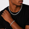 Man wearing a silver chain necklace and bracelet on a plain background