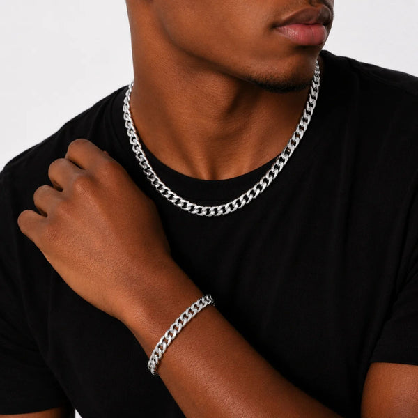 Man wearing a silver chain necklace and bracelet on a plain background