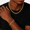 A close-up of a person wearing a thick gold Cuban link chain necklace and a matching gold bracelet, paired with a black t-shirt against a light gray background.