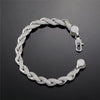 A silver-toned braided chain bracelet with pavé-set clear stones, featuring a lobster clasp and matching round end caps, displayed on a dark reflective surface.