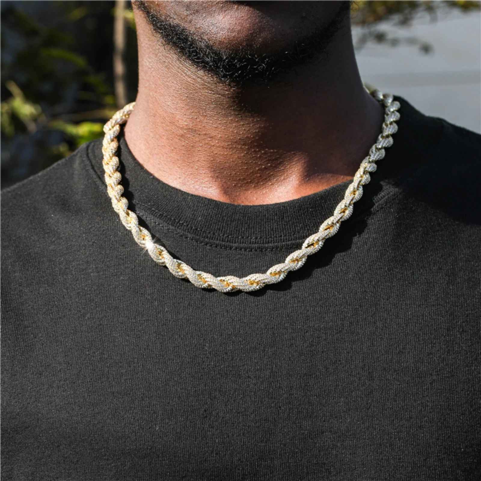 A close-up of a man wearing a thick rope gold chain necklace over a black t-shirt.