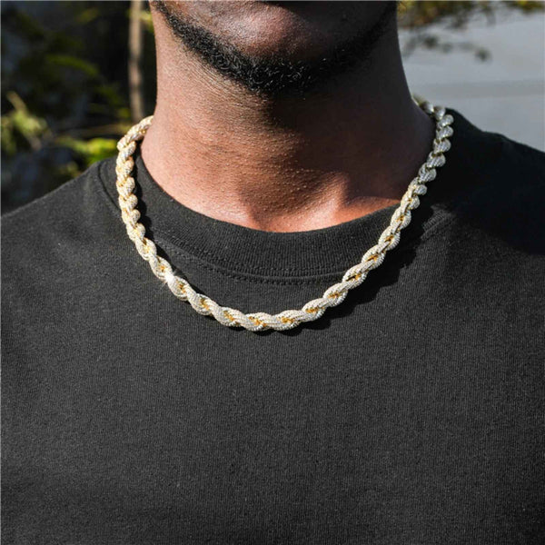 A close-up of a man wearing a thick rope gold chain necklace over a black t-shirt.