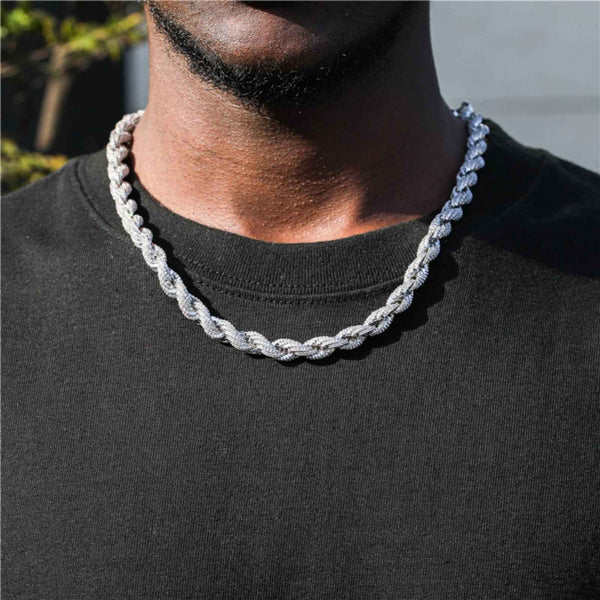 A close-up of a man wearing a thick, silver-toned rope style chain necklace over a black crewneck t-shirt.