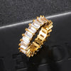A gold-plated eternity ring featuring a row of clear rectangular baguette-cut cubic zirconia, displayed on a textured black surface.