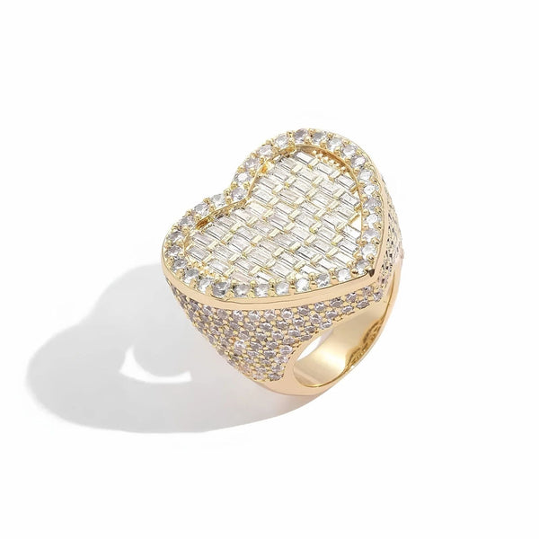 A heart-shaped gold ring pavé-set with clear baguette and round stones, photographed on a clean white background with a soft shadow.