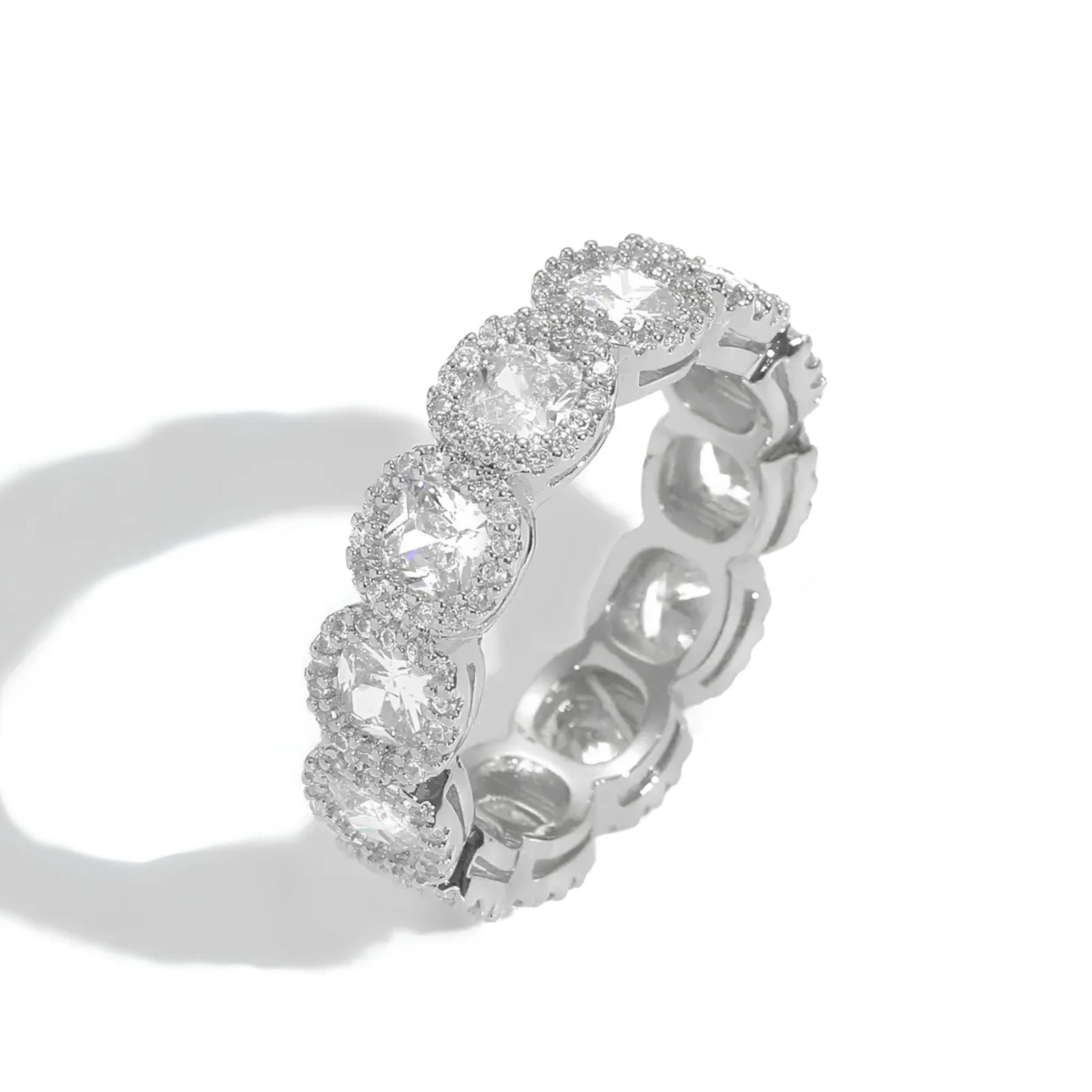 A silver-toned eternity ring featuring a row of round-cut clear cubic zirconia surrounded by small halo accents, photographed on a clean white background with a soft shadow.
