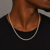 A close-up of a man's neck and upper chest wearing a tennis chain necklace with clear stones, paired with a black t-shirt against a neutral gray background.