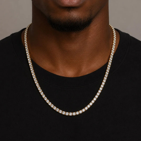 A close-up of a man wearing a gold-toned tennis chain necklace paved with clear cubic zirconia stones, styled over a black t-shirt.