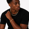 Man wearing a black t-shirt and gold toned jewelry on a plain background
