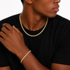 Person wearing a gold tennis necklace and bracelet on a plain background