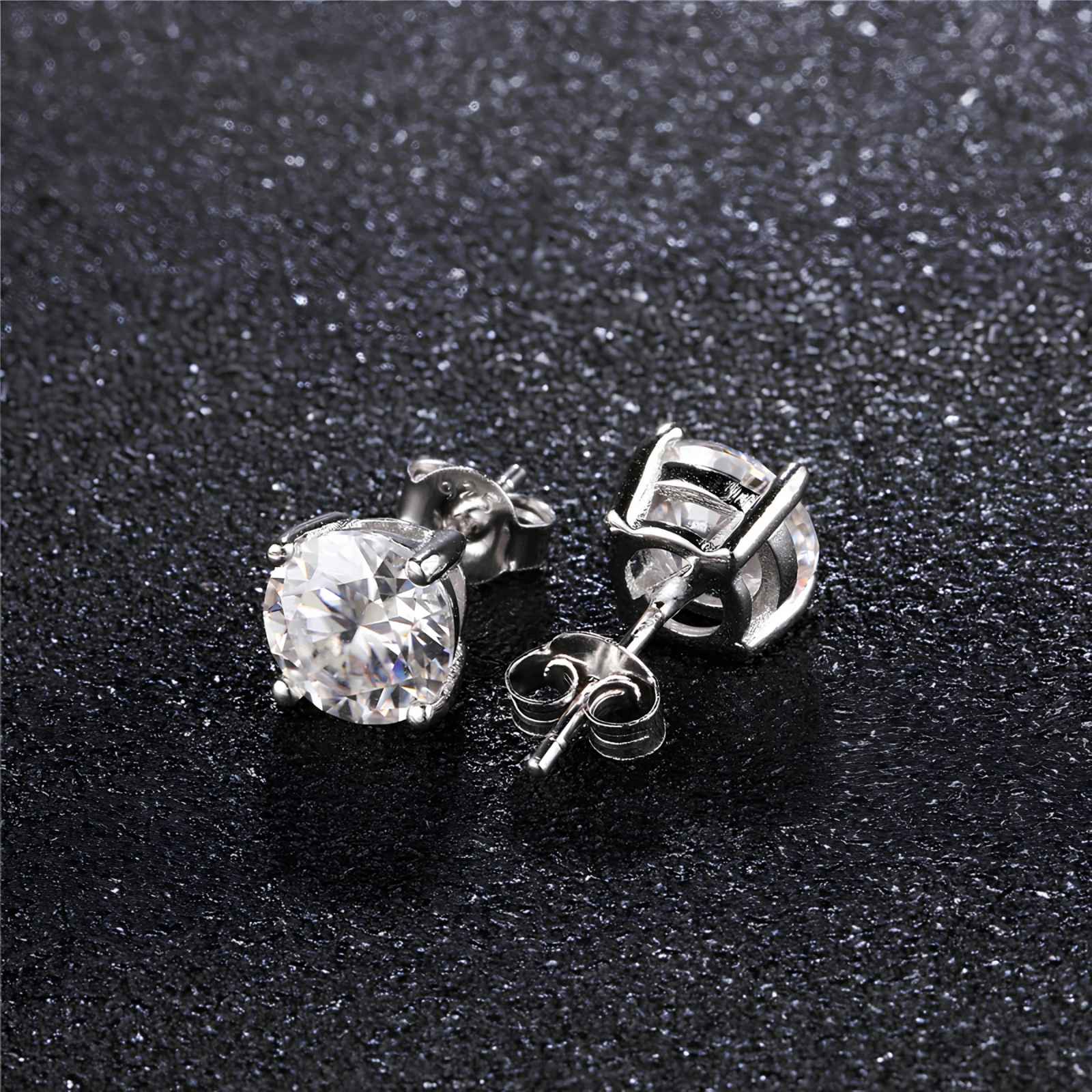 Silver stud earrings with a clear moissanite stone on a black textured background