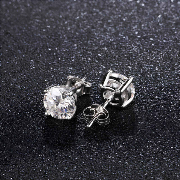 Silver stud earrings with a clear moissanite stone on a black textured background